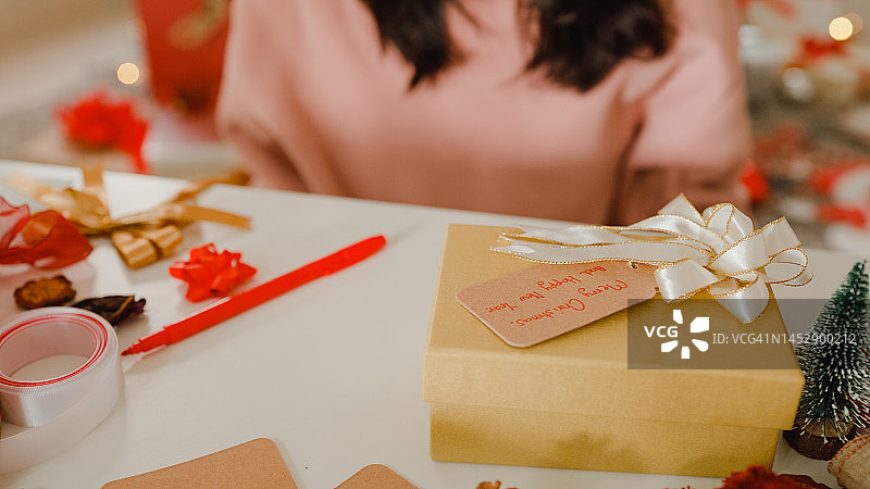 在家里的桌子上，女人用圣诞礼品盒写贺卡的特写。图片素材