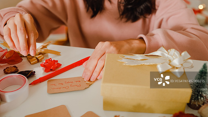 在家里的桌子上，女人用圣诞礼品盒写贺卡的特写。图片素材