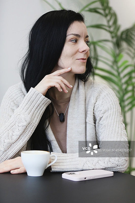肖像年轻的成年黑发女子放松在咖啡馆和看向别处图片素材