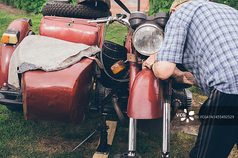 老人在夏天的院子里修理复古摩托车图片素材