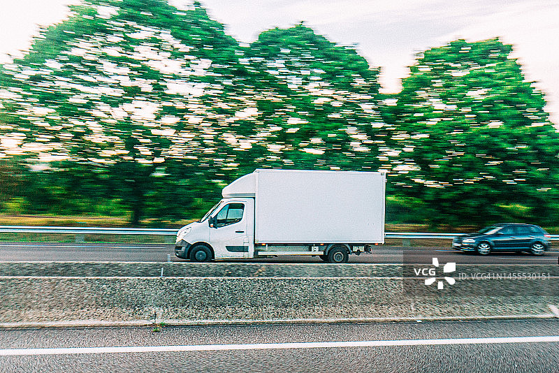 运动模糊小箱卡车行驶在法国北部的卡昂附近的a13高速公路上，在一个阳光明媚的夏天图片素材