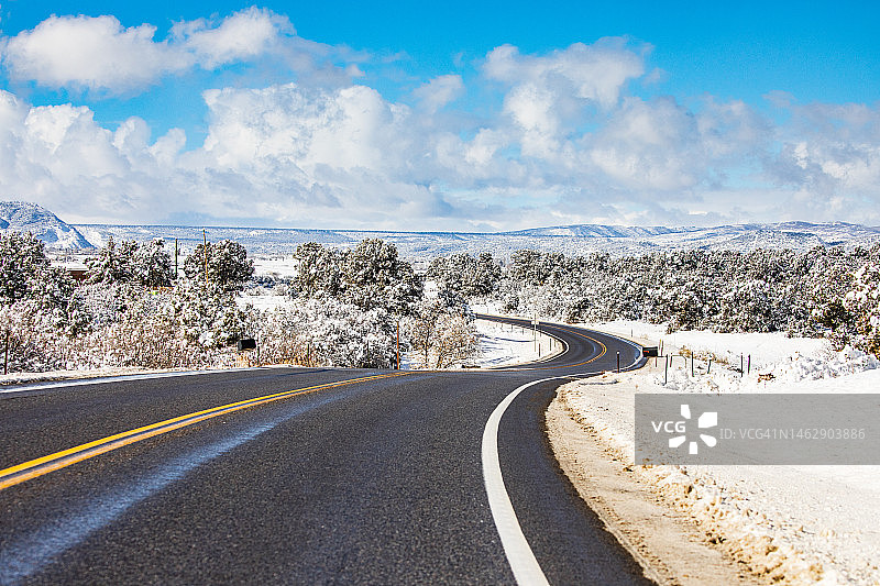 开阔的乡村道路被雪包围，背景是雪山图片素材