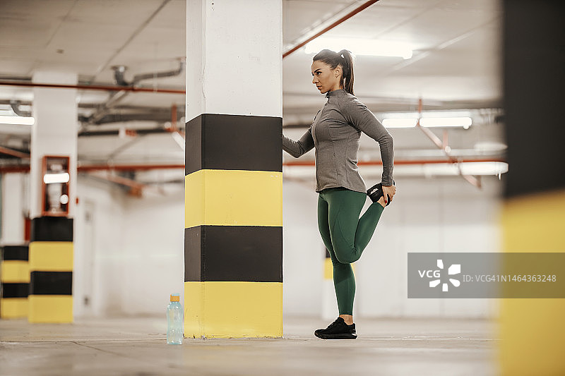 一位健康的女运动员正在地下车库里伸展她的腿，锻炼身体。图片素材