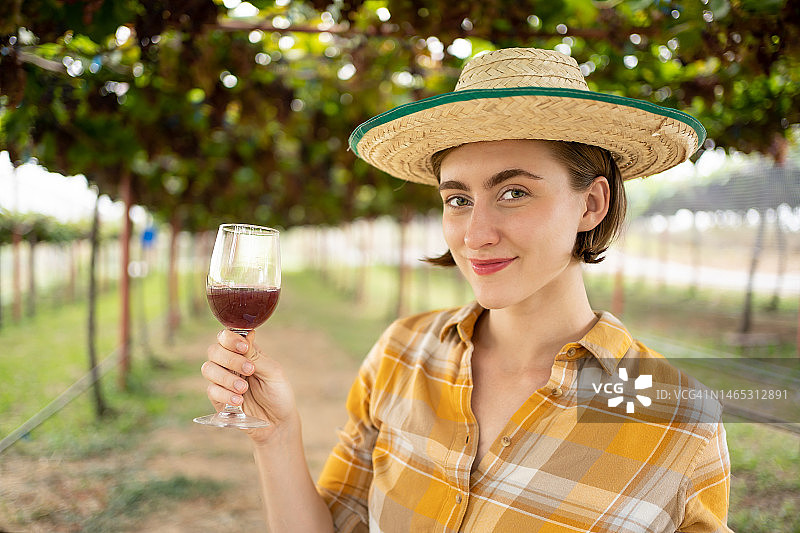 年轻快乐的白种人俄罗斯女人与绿色的眼睛品尝葡萄酒在葡萄田。快乐迷人的女性在葡萄园享受一杯葡萄酒。图片素材