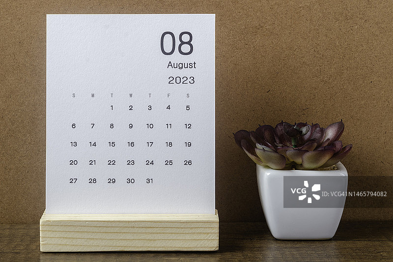 日历桌2023:8月是组织者计划和截止日期的月份，在牛皮纸背景下放置室内植物。图片素材