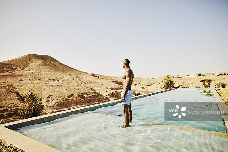 在沙漠营地放松时，男子站在泳池里的广角镜头图片素材