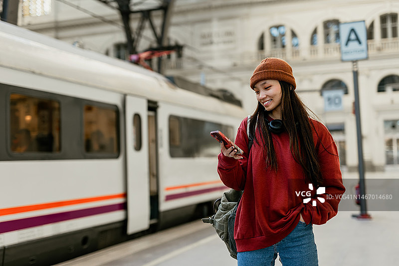 年轻时髦的亚洲女人在火车站用智能手机图片素材