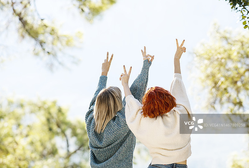 两个年轻女子举起手臂在大自然中玩的后视图图片素材