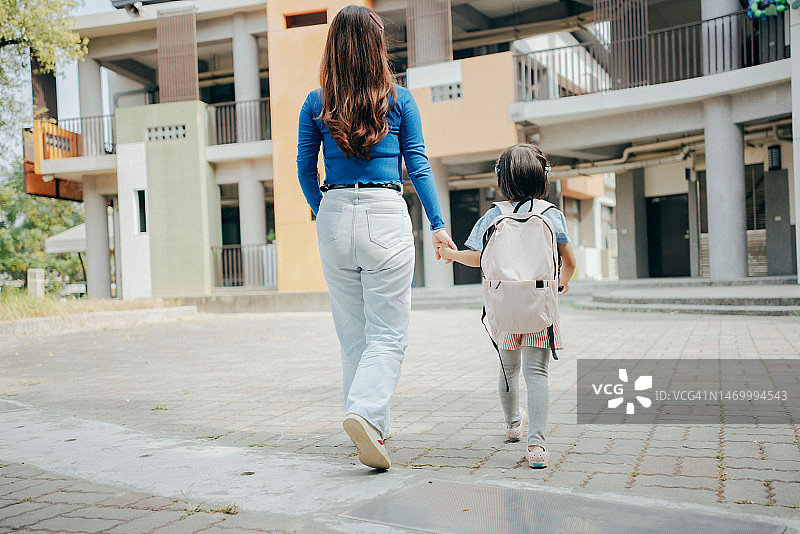 一位母亲牵着孩子的手走进校园，送孩子上学，准备开始崭新一天的学习之旅。图片素材