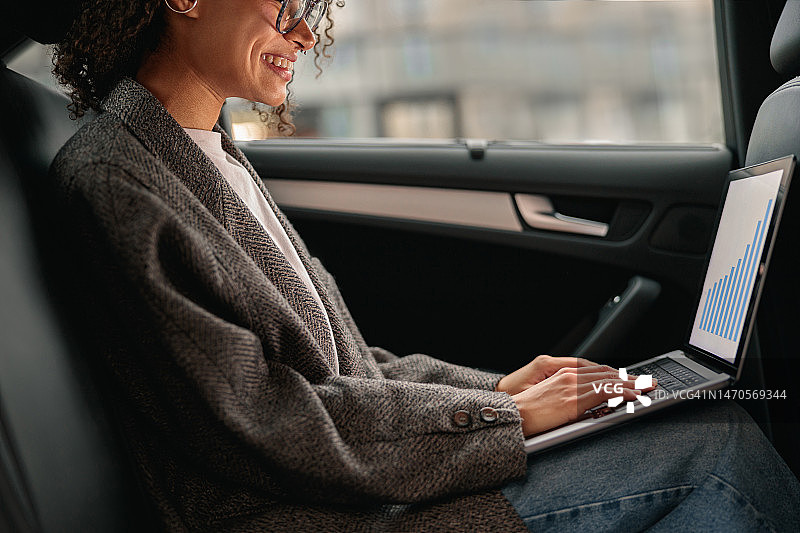 微笑的女分析师在笔记本电脑上工作，坐在汽车皮革后座去办公室的路上图片素材
