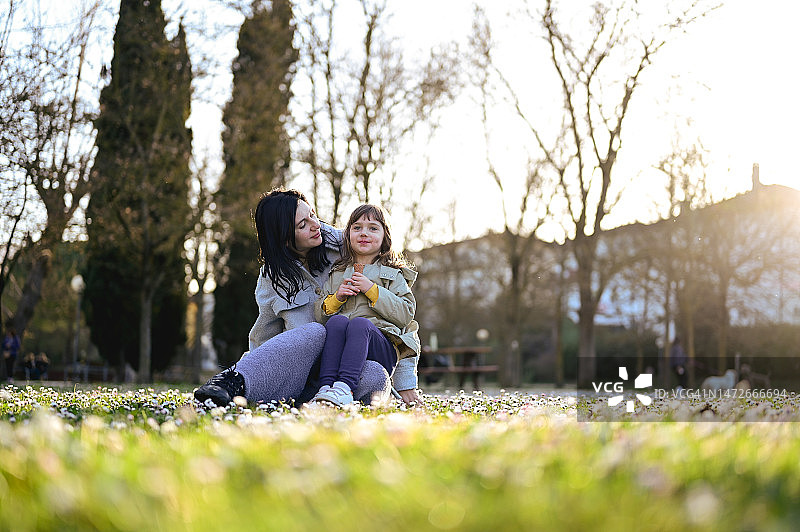早春的户外，母亲和女儿坐在绿色的草地上。图片素材
