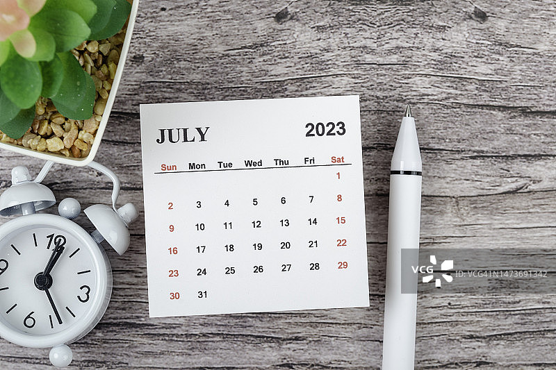 日历桌2023:7月是组织者在木桌背景上用闹钟和白笔做计划和截止日期的月份。图片素材