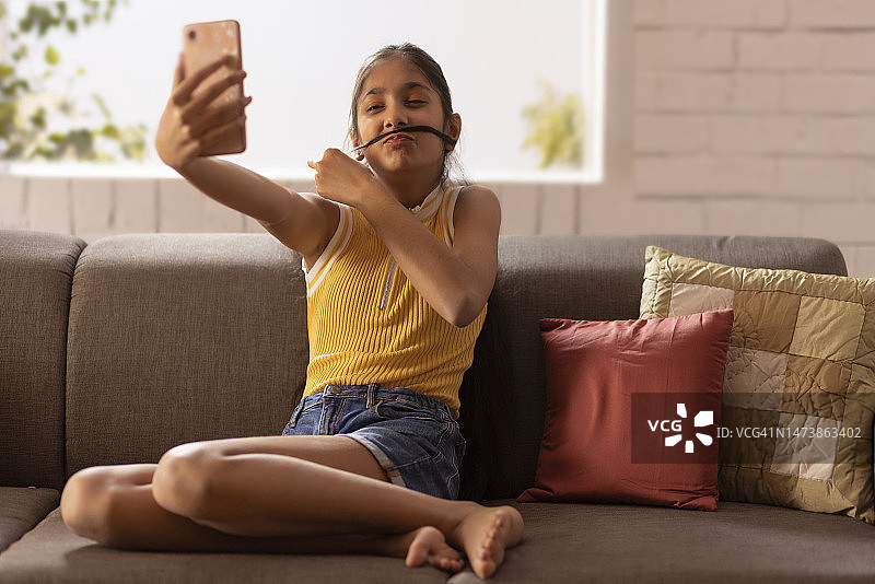 十几岁的女孩在用手机自拍时用她的头发做胡子图片素材