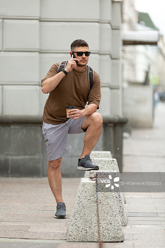 俄罗斯，一名男子站在大街上，手里拿着一次性咖啡杯，正在打电话图片素材