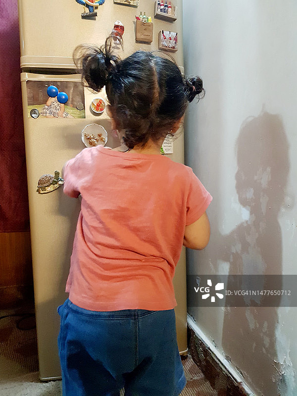 一个小女孩在家里忙着装饰冰箱门的后视图。图片素材