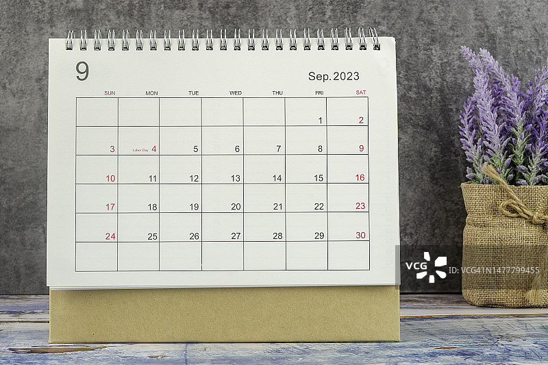 2023日历台:9月是组织者计划和截止日期的月份，在混凝土墙背景的木桌上手工制作一朵花。图片素材