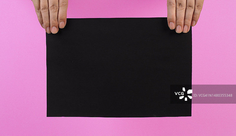手拿着粉红色背景的A4黑色纸板。图片素材