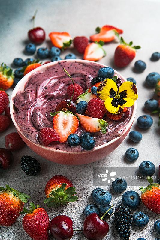 两碗夏季巴西莓冰沙配草莓和蓝莓，背景是灰色混凝土。早餐碗里有水果和麦片，特写，俯视图，健康食品图片素材