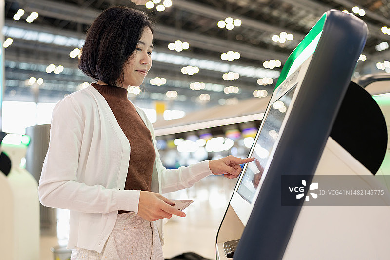 信息安全可以利用技术进行系统的控制和存储。亚洲旅行妇女在自动值机亭办理登机手续。触摸屏，选择航班详情，插入护照，在系统中记录数据，生成登机牌。图片素材