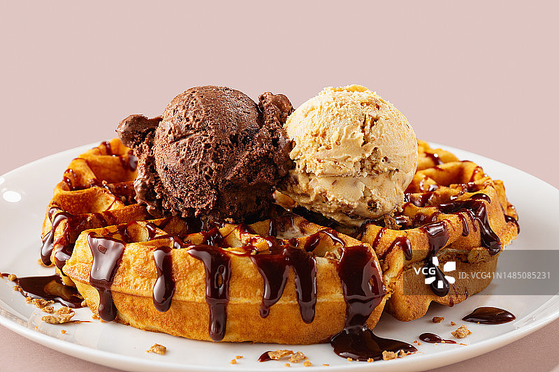 两球巧克力和焦糖冰淇淋放在比利时华夫饼上，特写，粉红色背景图片素材