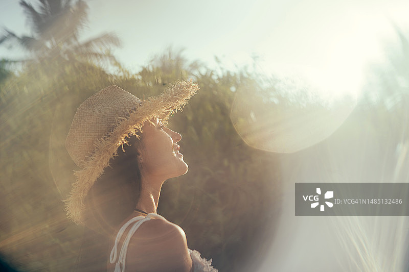 戴着太阳帽的女人在热带度假胜地享受日出。广角，低角度图片素材