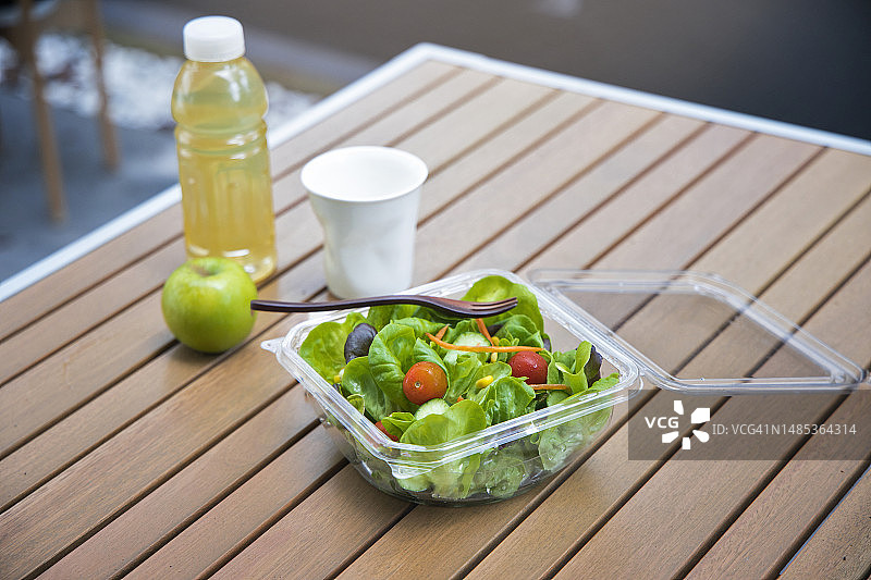 健康饮食带走塑料沙拉碗户外木制桌面。图片素材