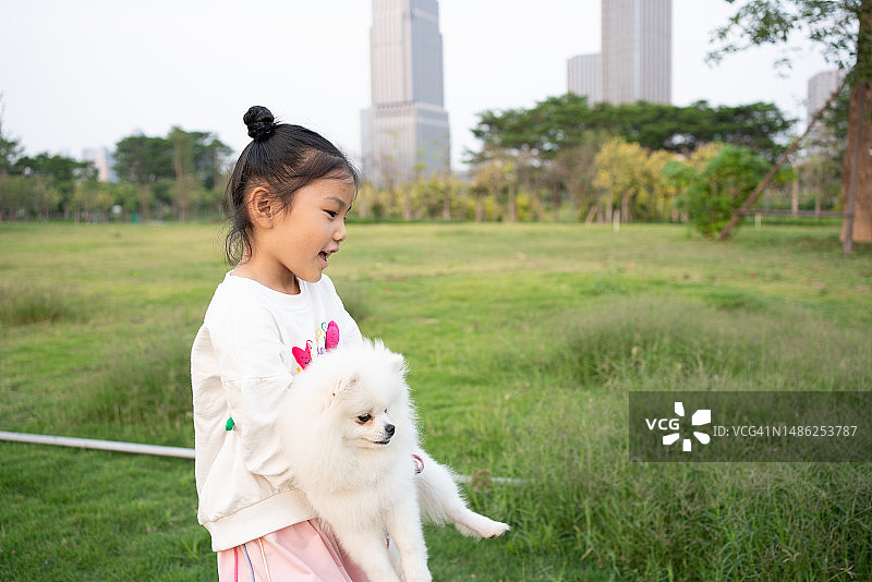 亚洲小女孩和波美拉尼亚狗在草地上散步图片素材