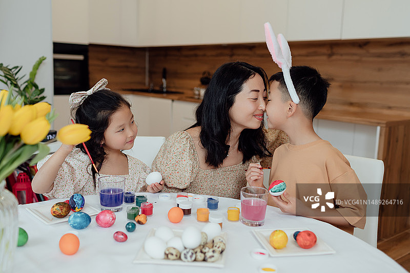 一个年轻的亚洲家庭，有两个孩子，一个男孩和一个女孩，坐在家里厨房的桌子旁画复活节彩蛋图片素材