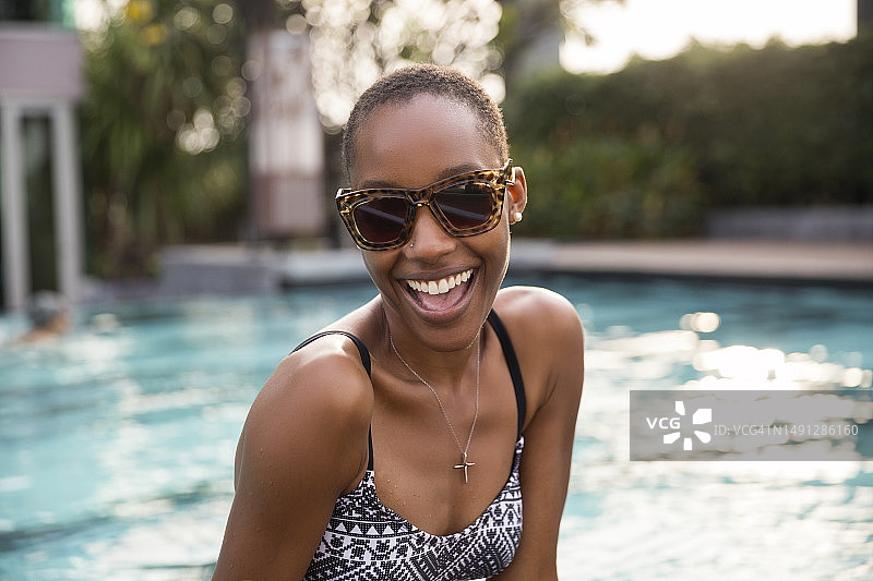 在度假胜地的游泳池边戴着墨镜的快乐女人图片素材