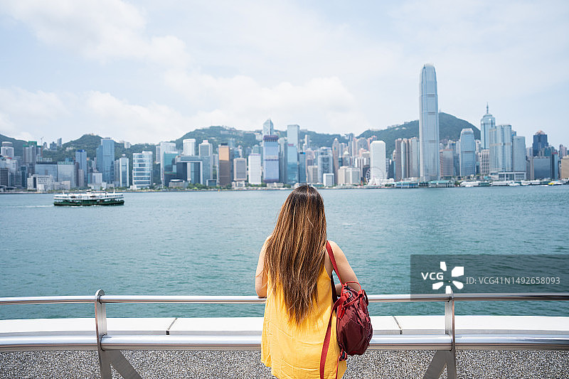 在香港一个阳光明媚的日子里，一位年轻的女游客拍摄了壮观的城市天际线。图片素材
