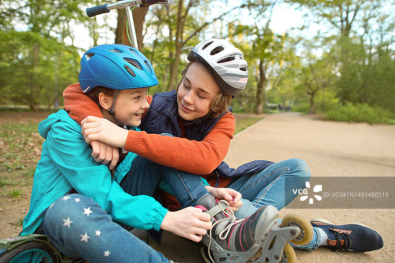 孩子们准备骑车:春天，一个男孩在公园里帮他的妹妹穿上旱冰鞋图片素材
