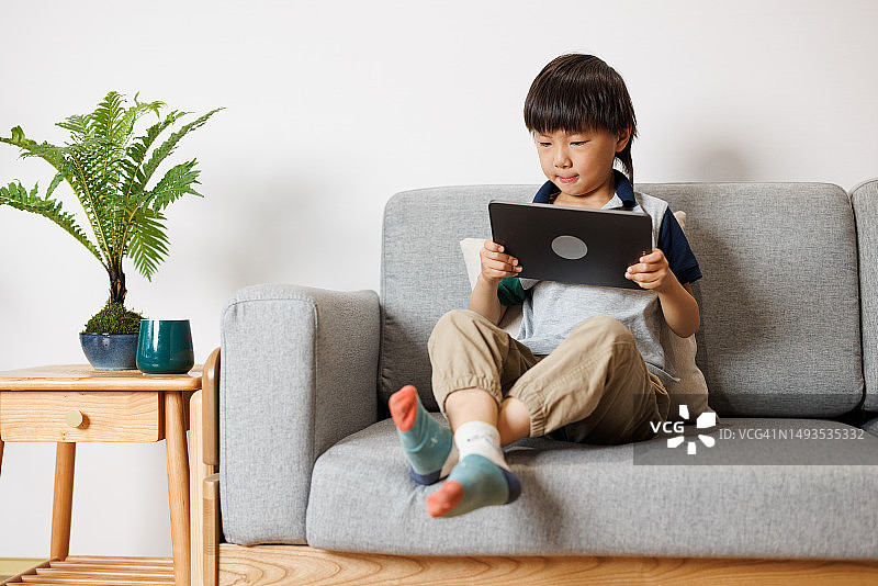 可爱的小男孩在家里的沙发上玩平板电脑图片素材
