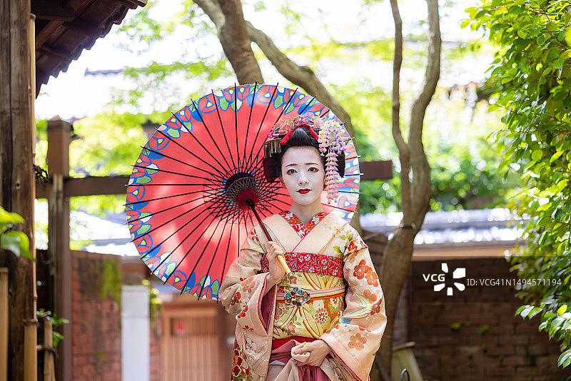 日本舞伎(艺伎训练)站在京都祗园狭窄的人行道上，用传统的日本纸伞遮阳图片素材
