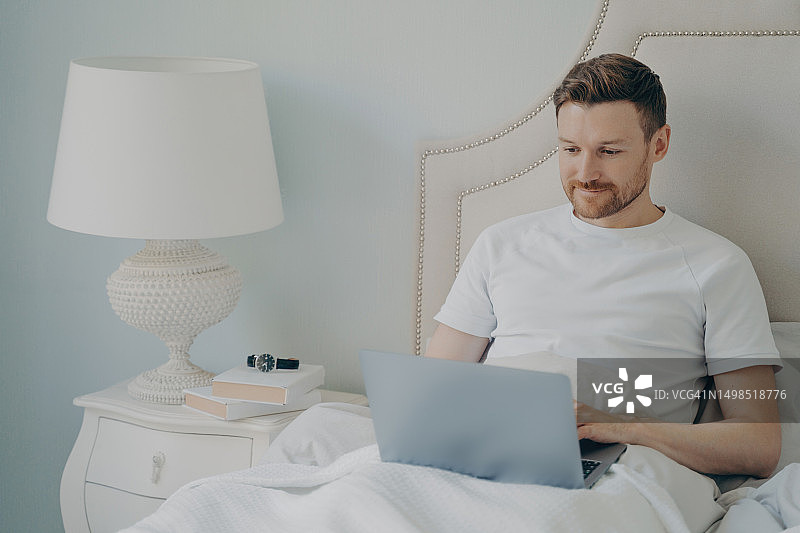 一个人坐在家里的床上玩笔记本电脑图片素材