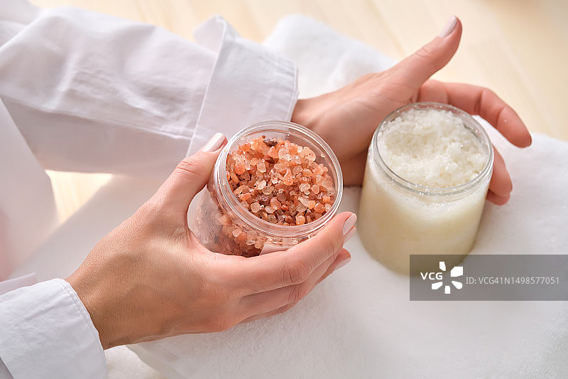 一罐喜马拉雅粉盐和女性手中的盐身体磨砂膏。图片素材