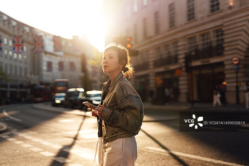 年轻的亚洲女子走在城市的大街上玩着智能手机图片素材
