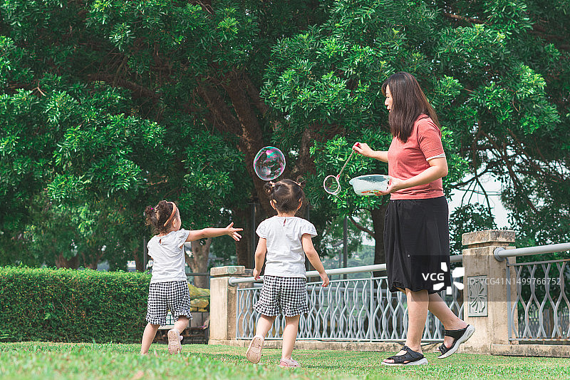 泡泡幸福:一位母亲带着双胞胎女儿玩耍的时刻图片素材