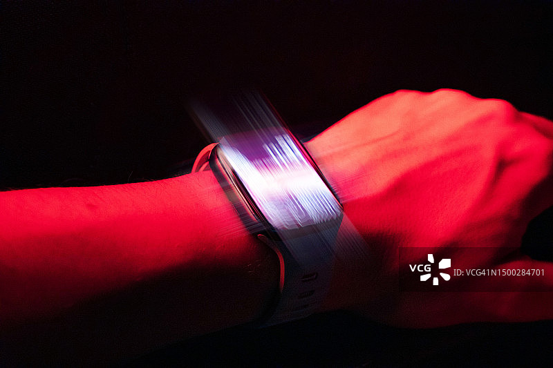 在黑暗的场景中，手腕上的未来智能手表会发出红光。图片素材