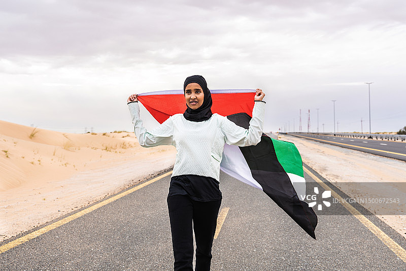 美丽的阿拉伯运动妇女戴着头巾在户外训练，手里拿着阿联酋国旗图片素材