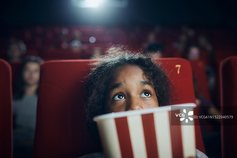 害怕的黑人女孩在电影院看电影。图片素材