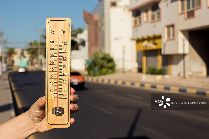 炎热的天气。热浪中，手持温度计站在城市前。高温概念图片素材