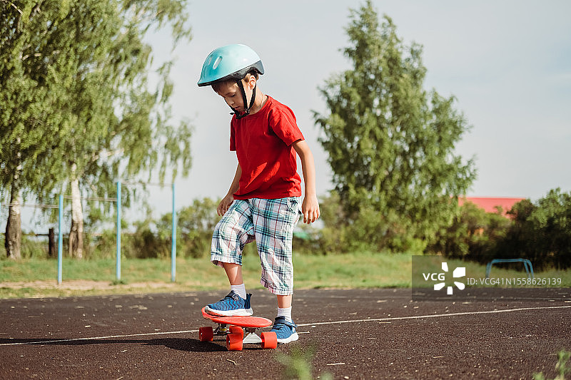 在一个阳光明媚的夏日，在一个滑板公园里，一个业余的小男孩在滑板上做出了第一次动作。初学者滑板者。图片素材