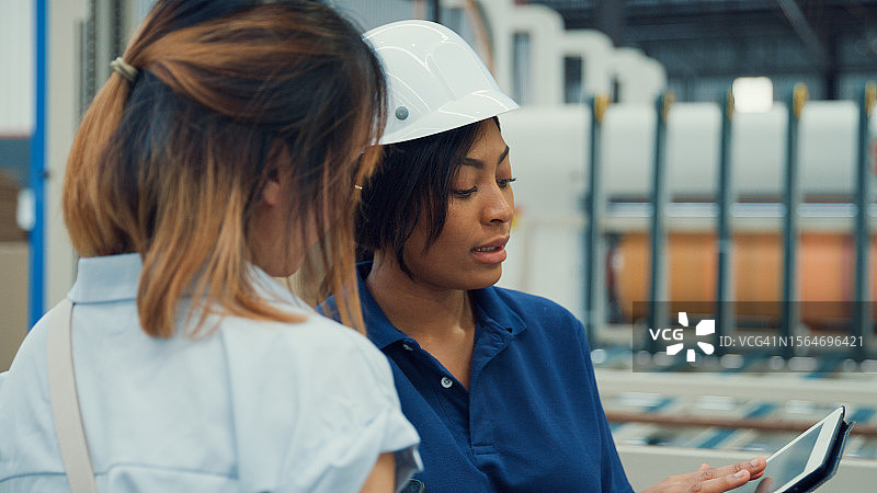 职业女性工业工程师在制造工厂使用平板电脑时与工厂工人交谈。在制造厂或生产厂工作。图片素材