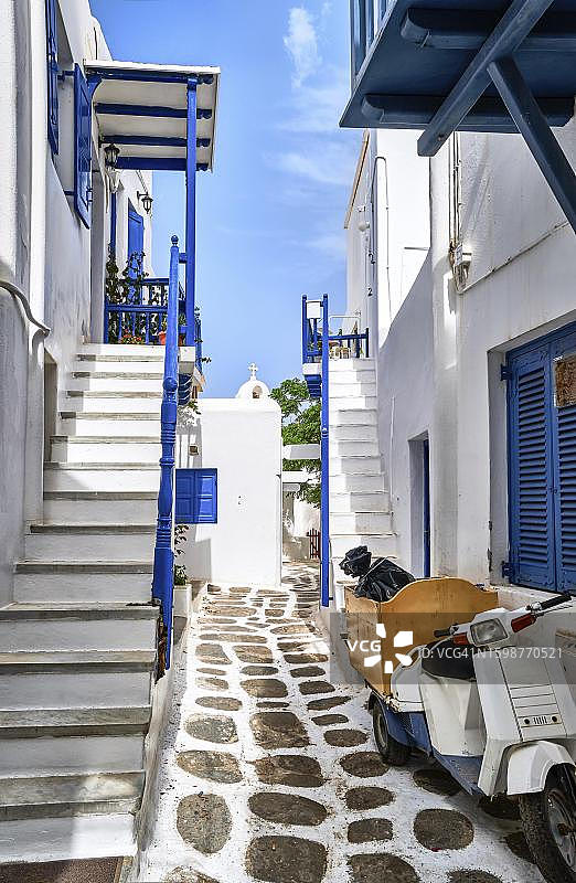 希腊岛屿城镇浪漫的传统狭窄街道和美丽的小巷。粉刷过的房子，蓝色的阳台，铁轨和新栅栏，鹅卵石铺成的人行道。停着的旧摩托车。米克诺斯,希腊图片素材
