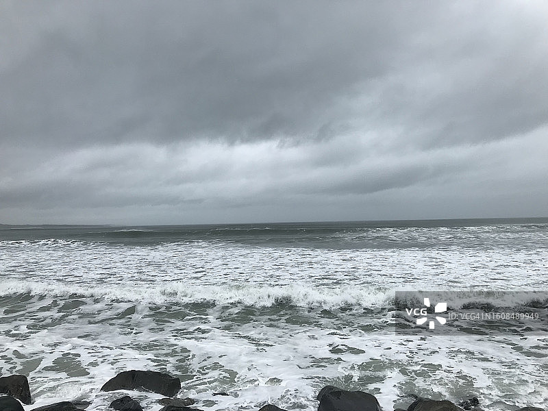 在斯莱戈的斯特兰德希尔，一个阴天，白色的泡沫海水倾泻在岩石海岸线上图片素材