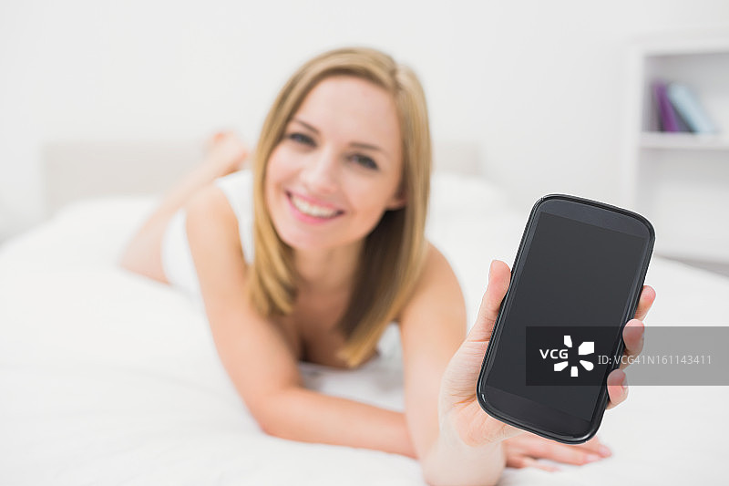 女人在床上展示智能手机的肖像图片素材