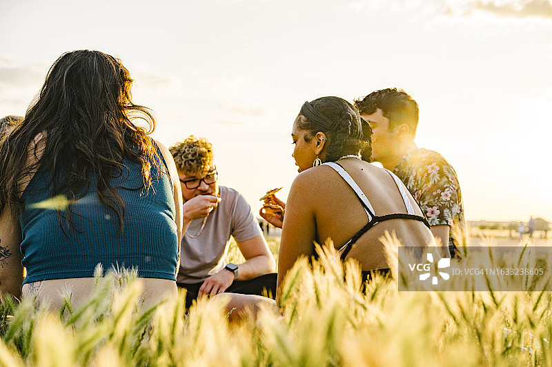 从背后看，一群朋友围成一圈，在傍晚的阳光下一起享用披萨图片素材