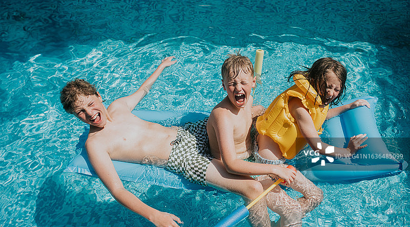 三个兄弟姐妹坐在泳池的浮子上——他们高兴地尖叫着图片素材