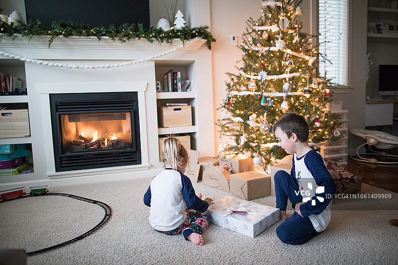 男孩和女孩一起在圣诞树下打开礼物图片素材