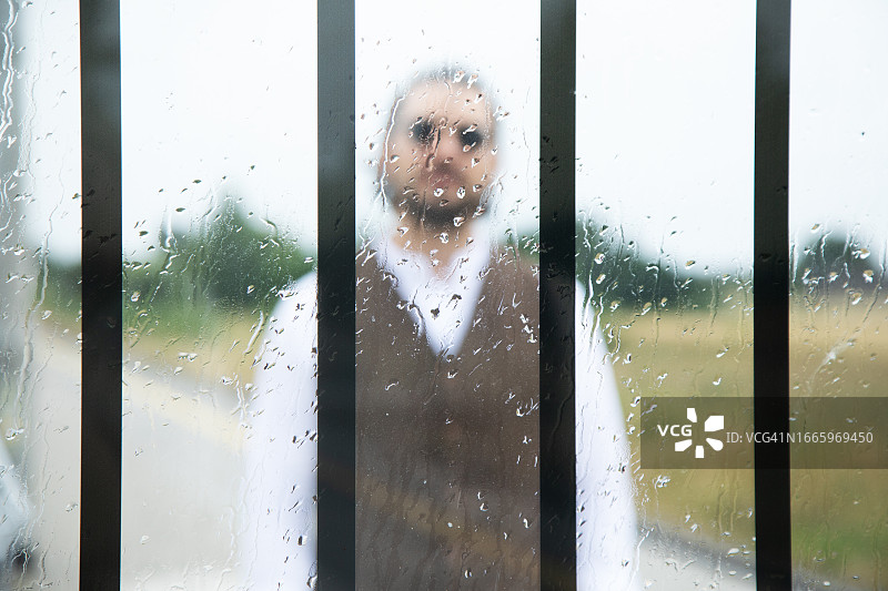 一名男子站在玻璃后面的模糊照片，上面有黑色的垂直线和雨滴图片素材